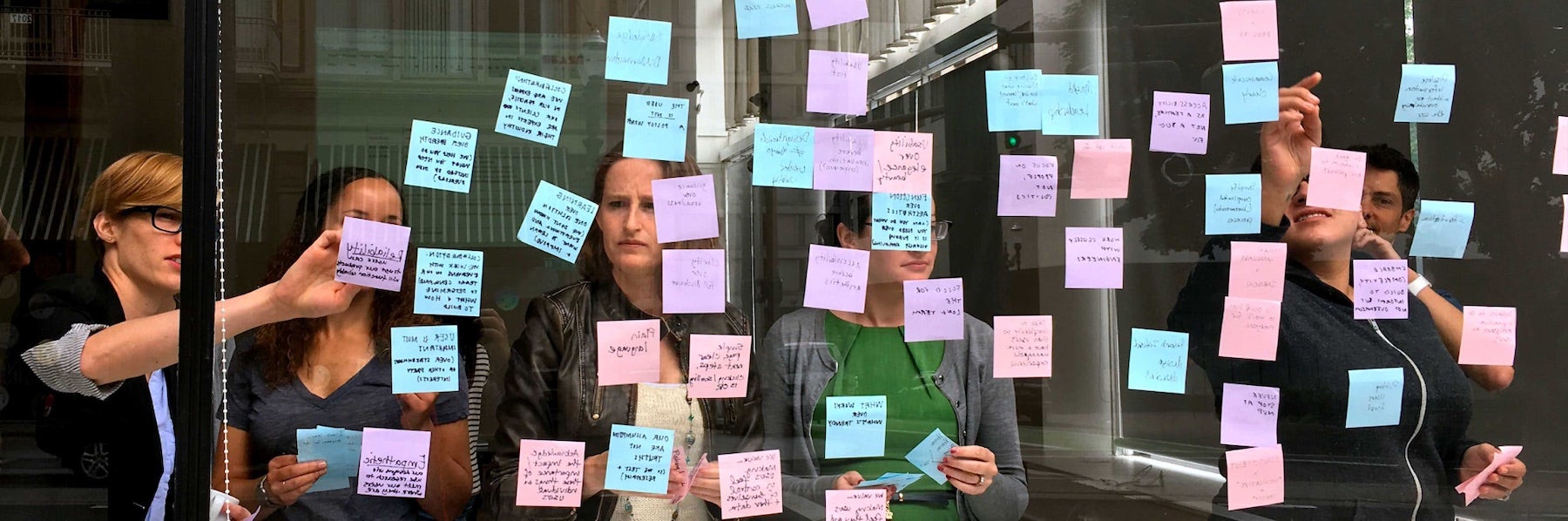 Ad Hoc staff pointing to a wall of Post-It notes on glass during an affinity mapping exercise.